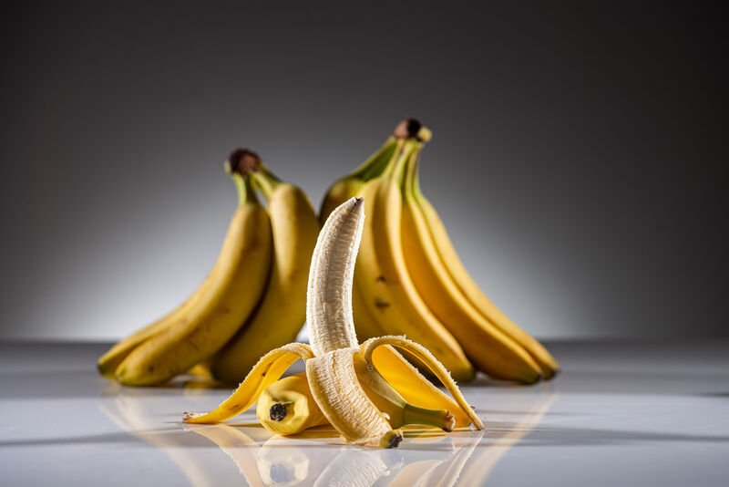 Stehende, halb geschälte Banane vor mehreren stehenden Bananen