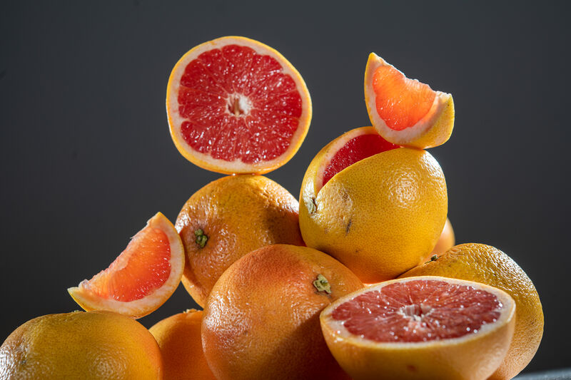 ein Stück einer Grapefruit auf ganzen und halbierten Grapefruits liegend