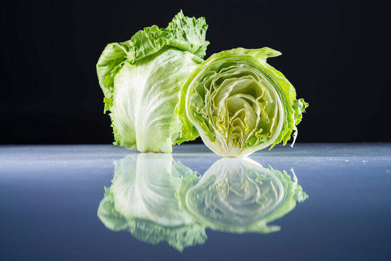 angeschnittener, halbierter Eisbergsalat-Kopf vor ganzem Eisbergsalat