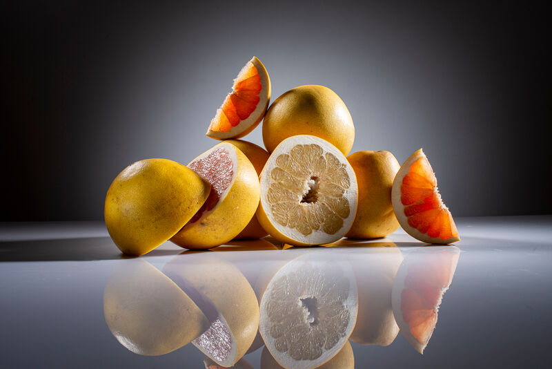 ein Stück Honigpomelo auf halbierten und ganzen Honigpomelos liegend