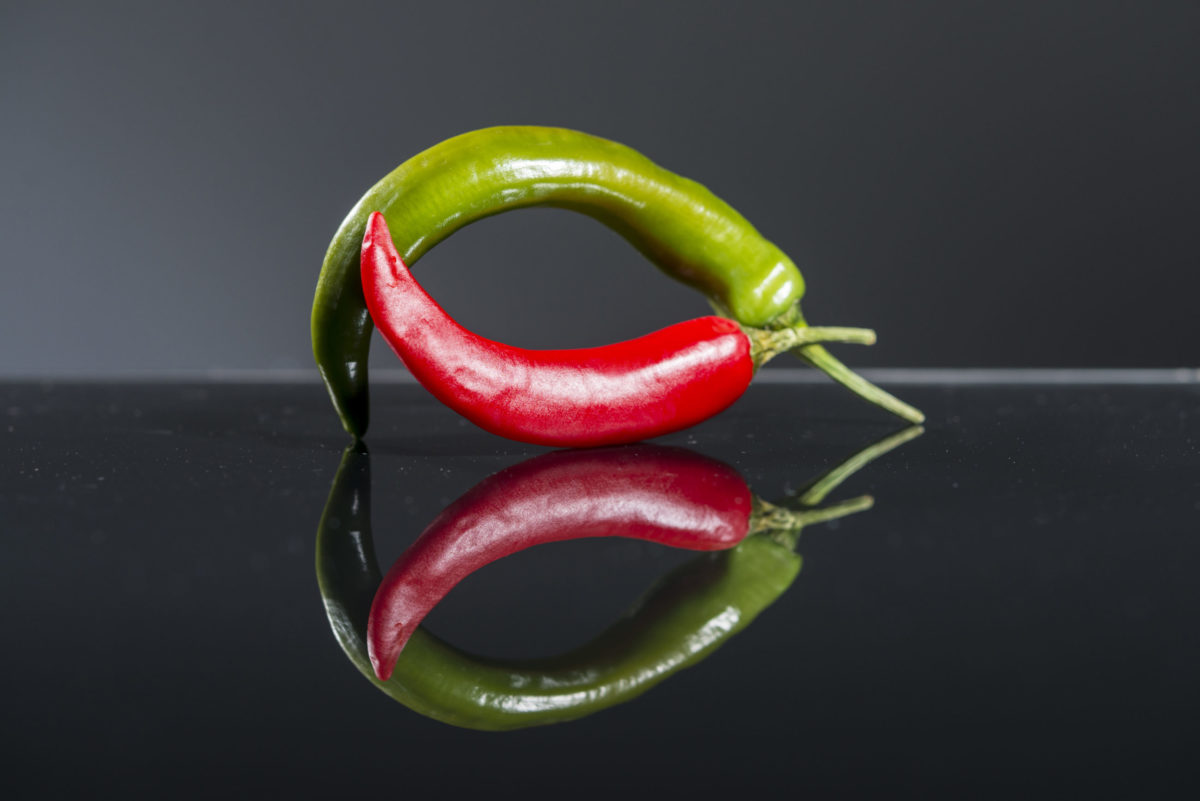 Eine grüne Peperoni (oben) und eine rote Peperoni (unten) bilden einen Kreis.