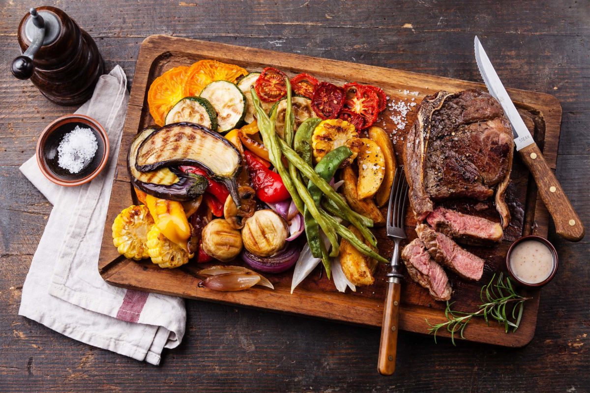 Hier gibt’s alles, was du grillst! Gegrilltes Gemüse und Fleisch auf Holzbrett drapiert