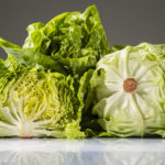 Angeschnittener, halbierter Kopfsalat-Kopf vor ganzen Kopfsalaten.