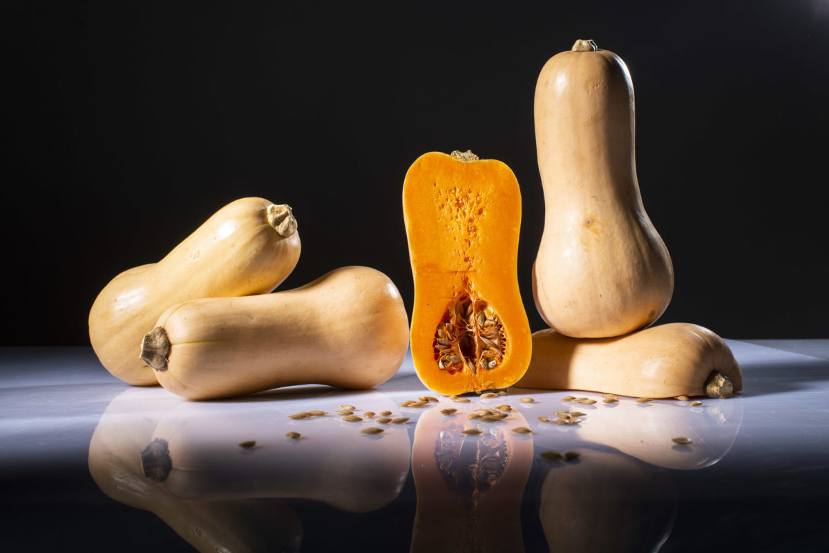 Butternutkürbis Butternutkürbis ganz und geschnitten vor schwarzem Hintergrund.