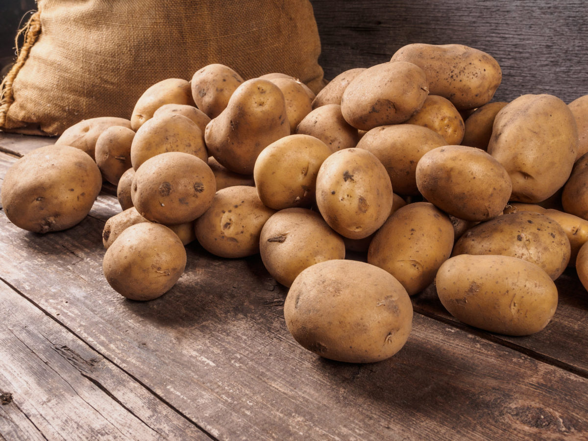 Kartoffel Kartoffeln liegen auf einem Holzboden vor einem Kartoffelsack.