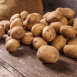 Kartoffeln liegen auf einem Holzboden vor einem Kartoffelsack.